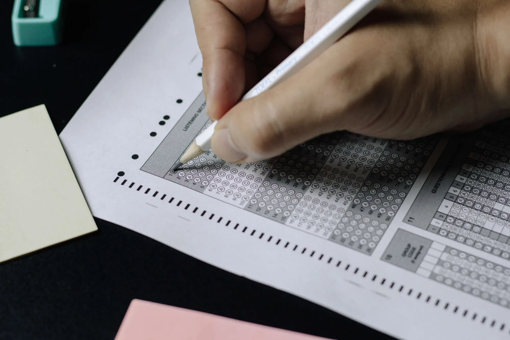 A photo of a hand holding a pencil and completing a sheet of multiple-choice questions.