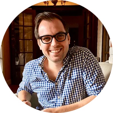 A photograph of a man called Andrew O'Malley. He is smiling at the camera. He wears a blue and white checked shirt and glasses. He is in an indoor setting.