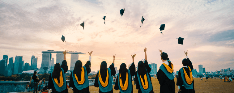 A photo of a group of graduating students in robes with their backs to the camera. They have all thrown their graduation caps into the air.